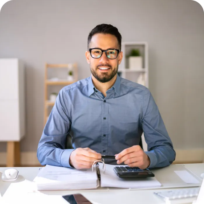 Man in glasses sitting at a desk with papers and a calculator.