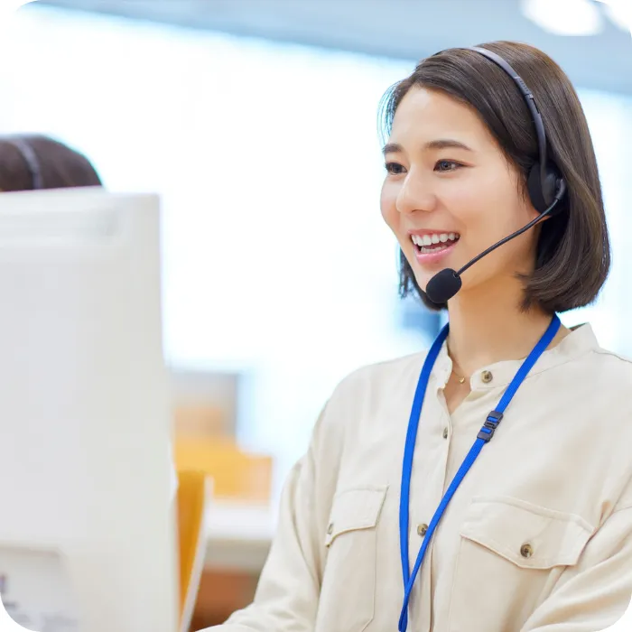 Smiling woman with headset at a computer, wearing a blue lanyard.