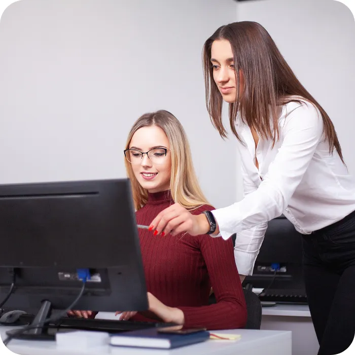 Two women working together at a computer in an office setting.