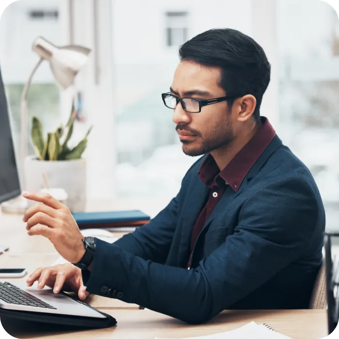 Man in glasses focused, pointing at computer in office setting.
