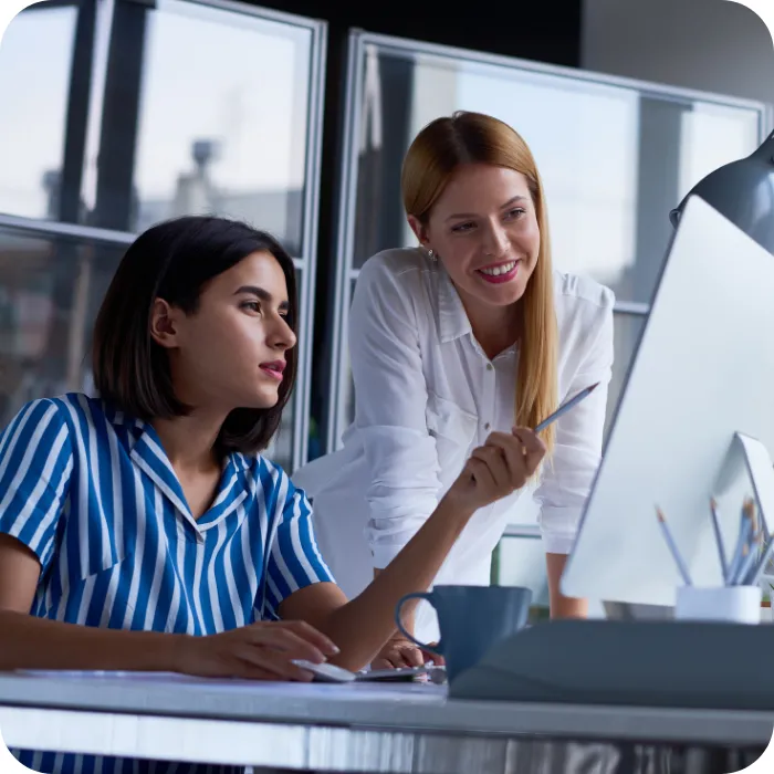 Two women collaborating at a computer, one pointing at the screen.