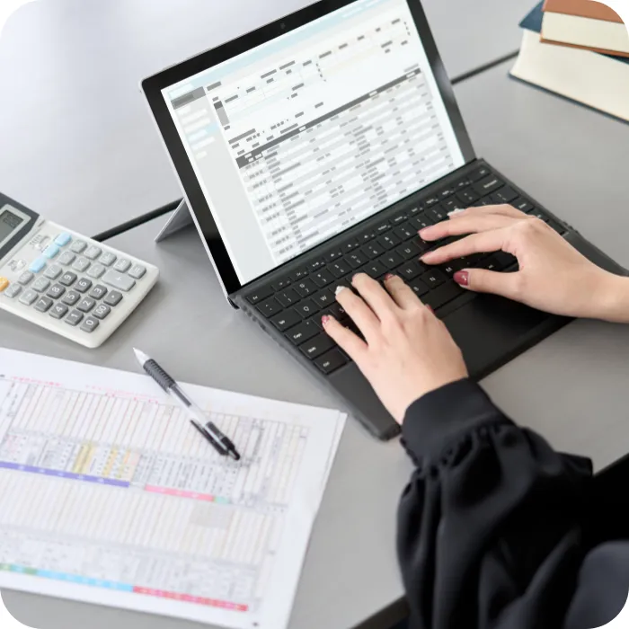 Hands typing on a laptop with spreadsheets, near a calculator and documents.