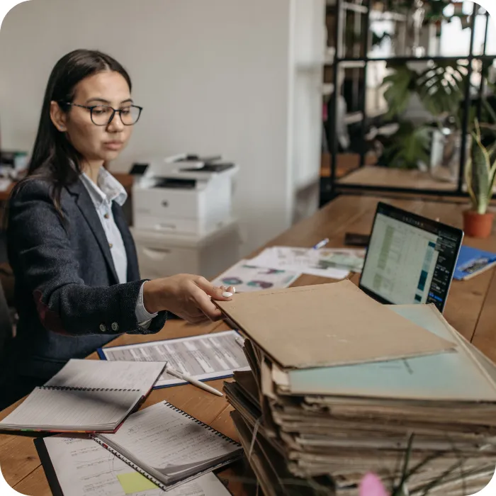 Person in office working at a cluttered desk with a laptop and papers.