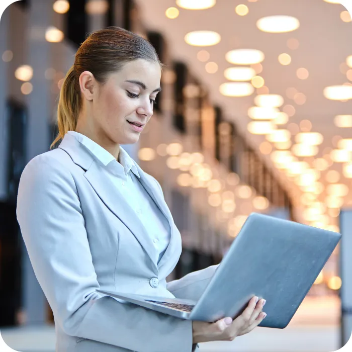 Woman in a blazer using a laptop in a brightly lit hallway.