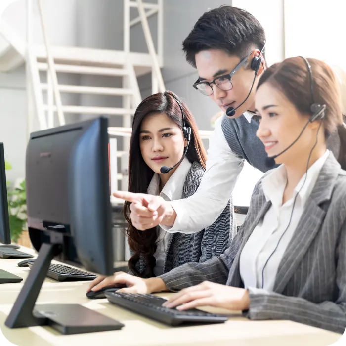 Three people with headsets working at computers in an office.