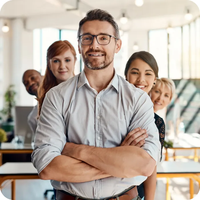 Smiling team in an office, man in front with folded arms.