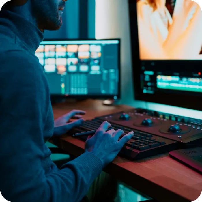 Person editing video on dual monitors in a dimly lit room.