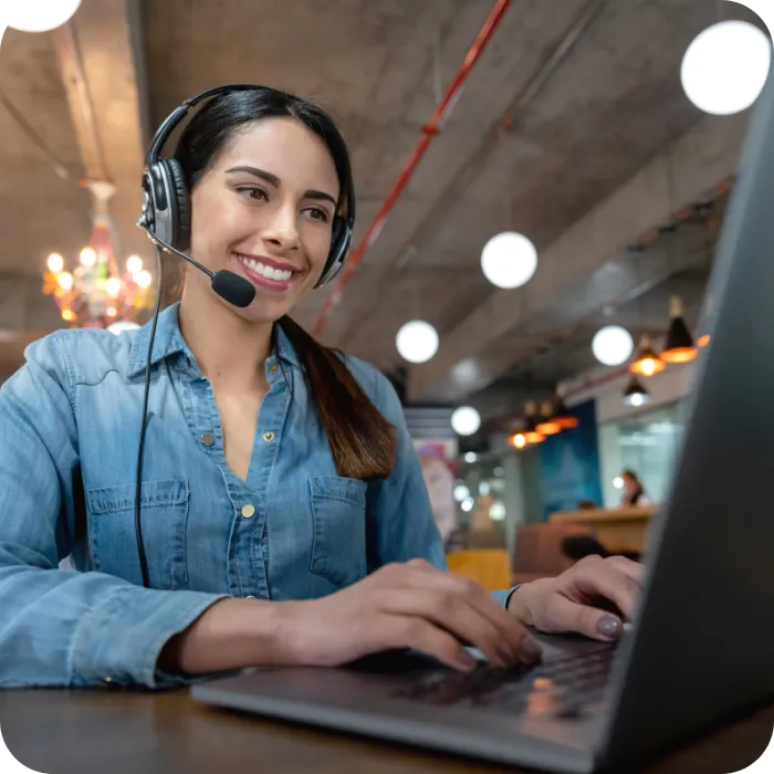 Smiling woman with headset typing on laptop in modern office.