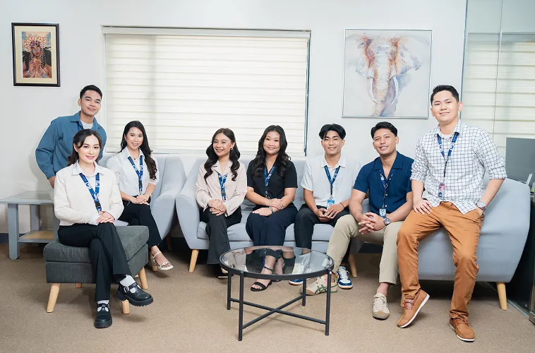 A group of eight people seated in an office, smiling at the camera.