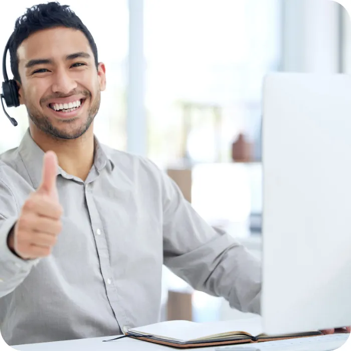 Smiling man with a headset giving a thumbs-up at his desk.