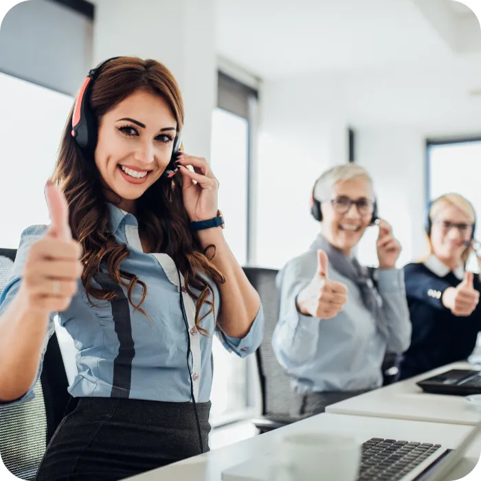 Call center employees smiling with thumbs up, wearing headsets.