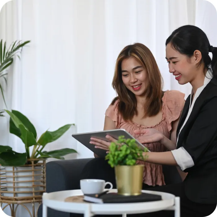 Two women smiling, looking at a tablet together indoors.