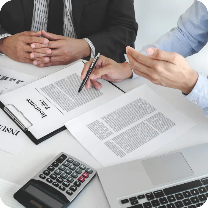 Two people discussing documents at a desk with a calculator and laptop.