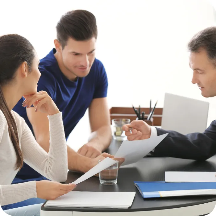 Three people discussing documents at a desk, appearing focused and engaged.