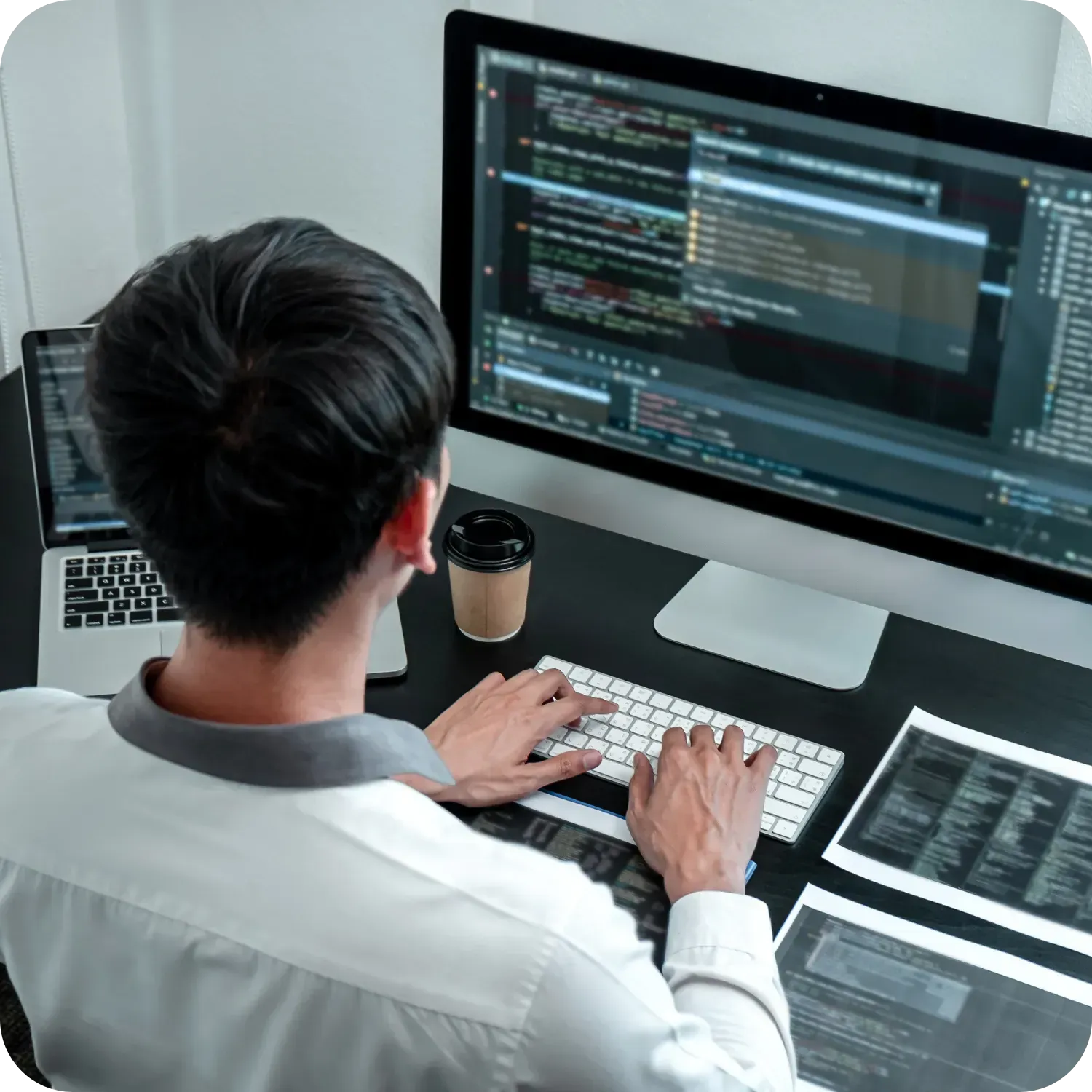 Person typing code on a computer at a desk, with multiple screens.