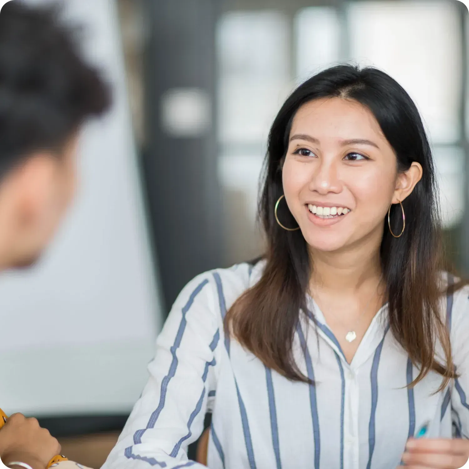 Woman smiling while talking to a blurred person, office setting.