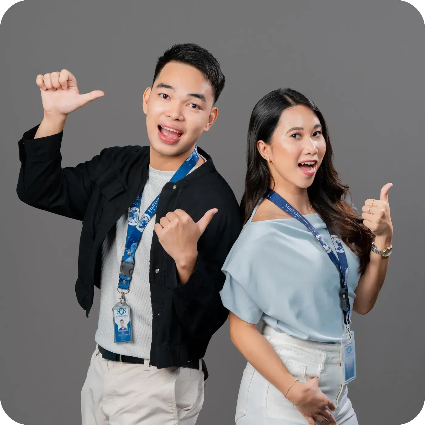 Two people smiling, giving thumbs up, wearing lanyards against a gray background.