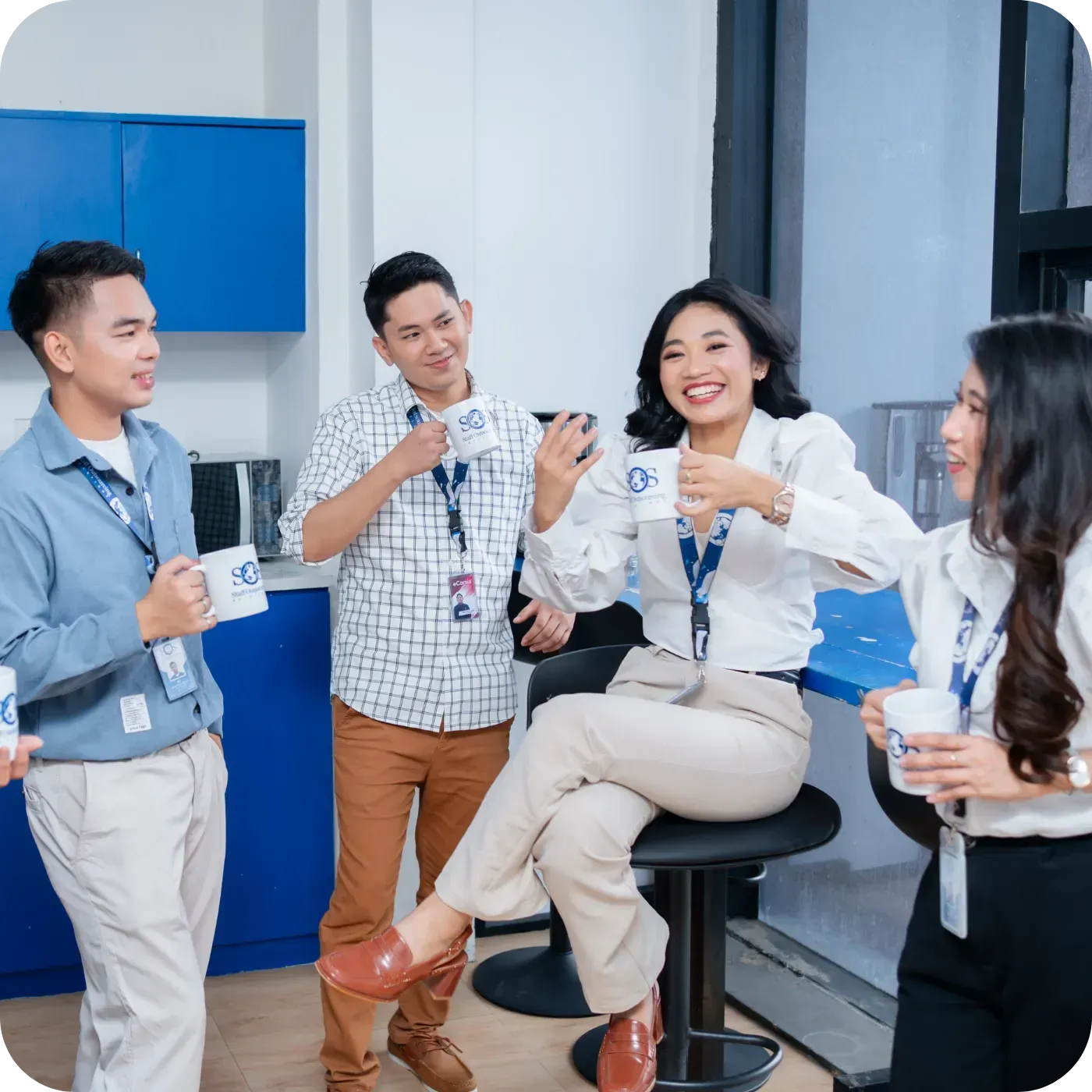 Office coworkers smiling and chatting over coffee in a bright break room.