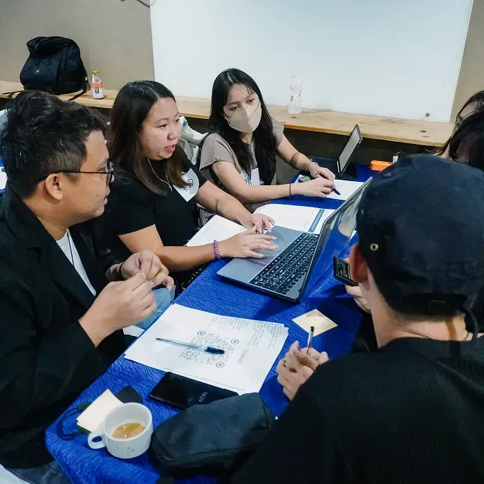 People collaborating around a table with laptops and papers.
