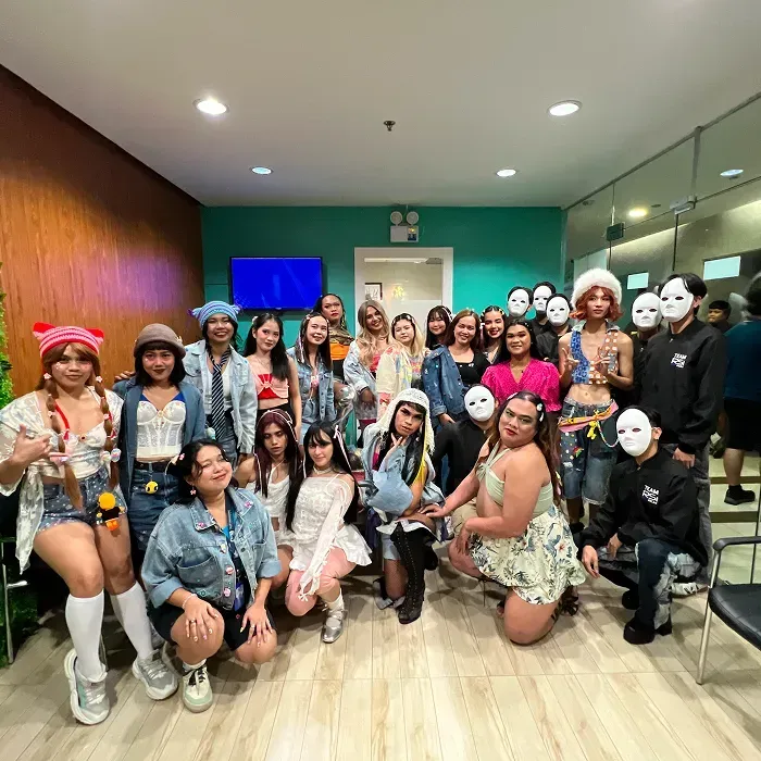 Group dressed in colorful costumes, some wearing masks, in a brightly lit room.
