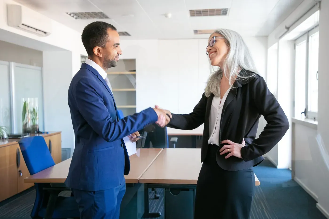 Two people shaking hands across a meeting room table