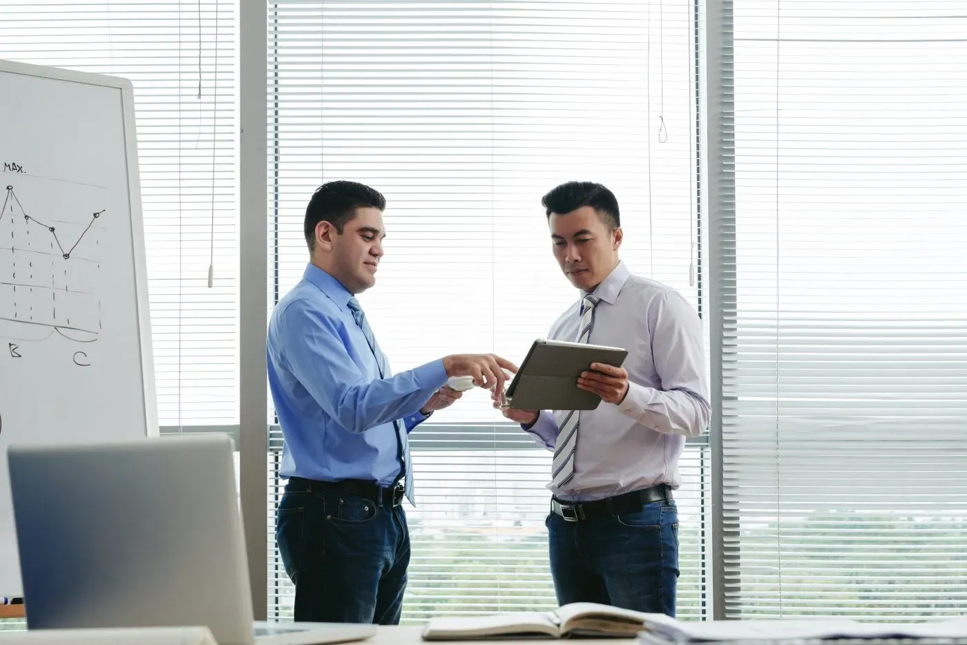 Two colleagues standing in an office reviewing figures together on a tablet
