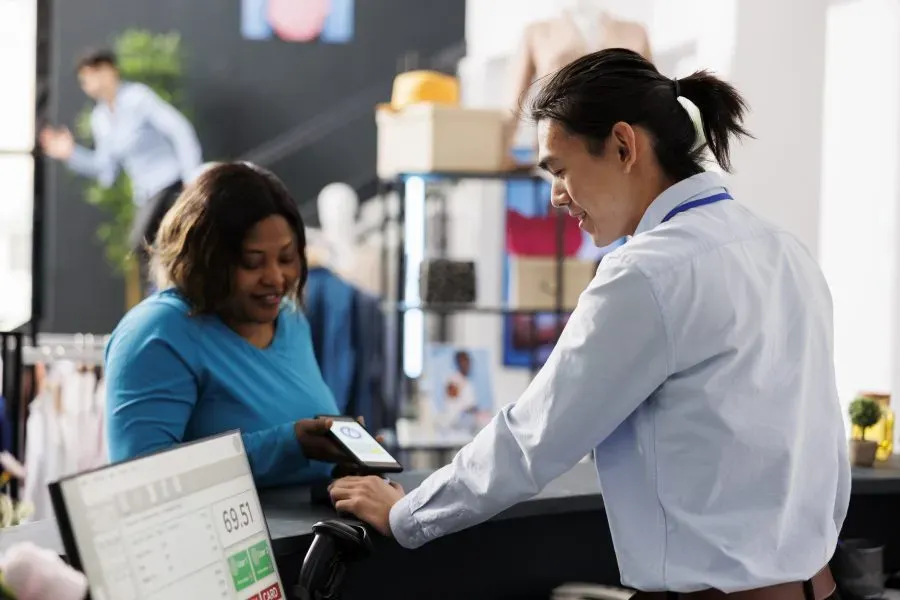 Shopper paying by phone at a clothing store counter while a sales assistant helps