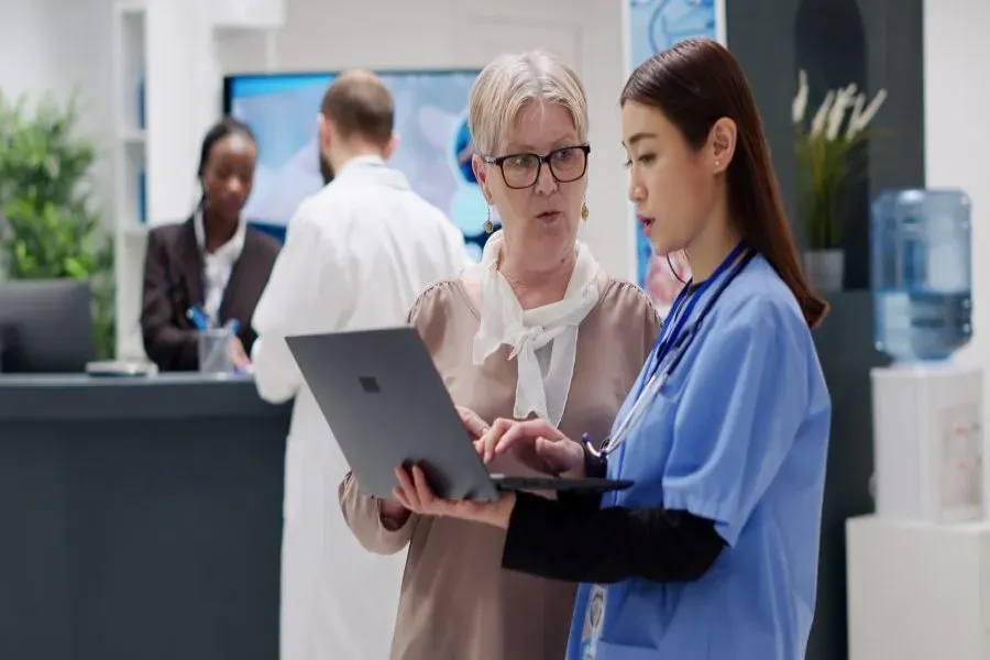 Medical assistant going through a report on a laptop with a patient at a hospital reception desk